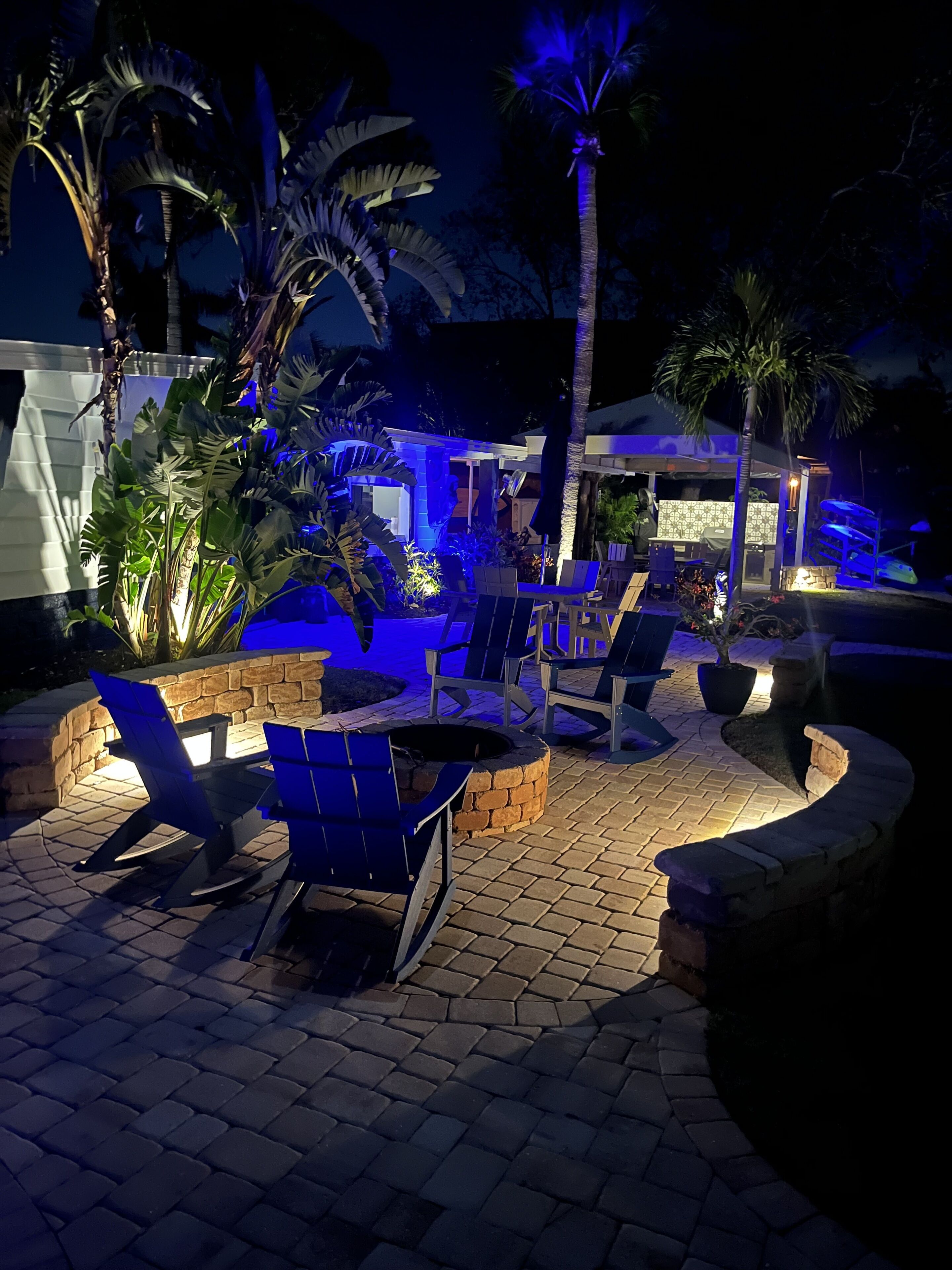 Ein Terrassenbereich im Freien mit Sitzgelegenheiten und einer Feuerstelle, umgeben von Pflanzen und einem Poolbereich.