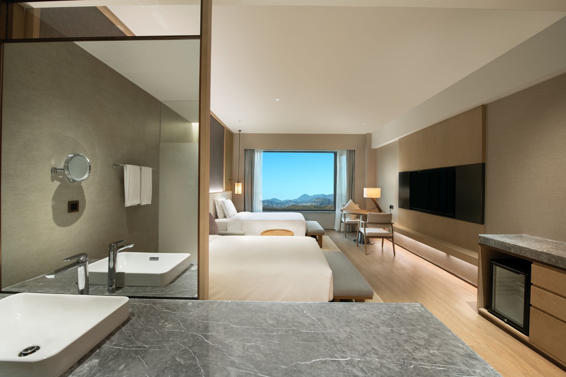 A modern hotel room with a large bed, a desk, a TV, and a bathroom with a sink and mirror.