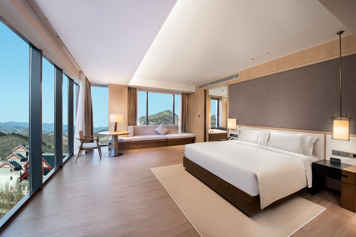 A modern hotel room with a large bed, a seating area, and a view of the mountains.