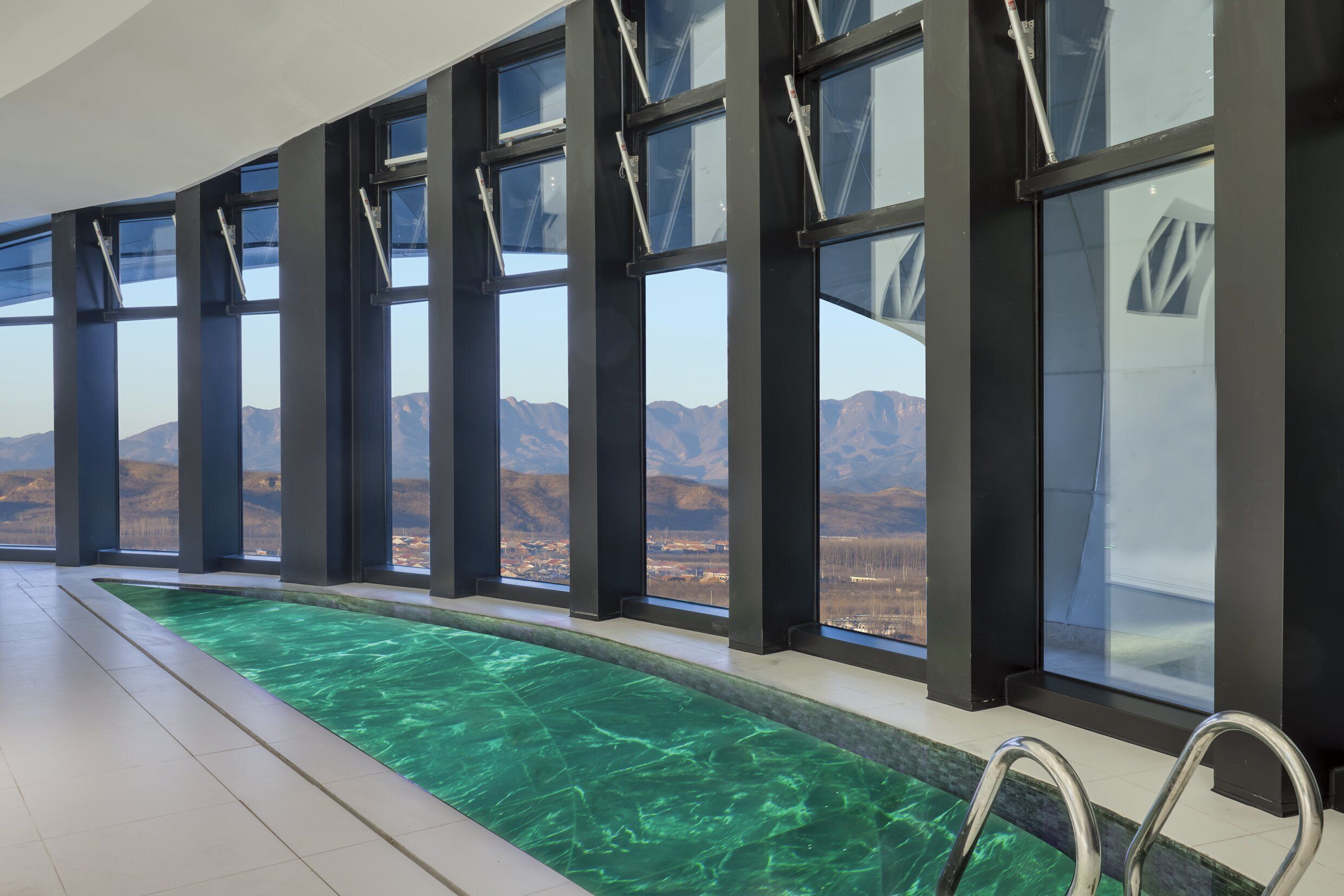 A swimming pool with clear water, surrounded by large windows offering a view of mountains.