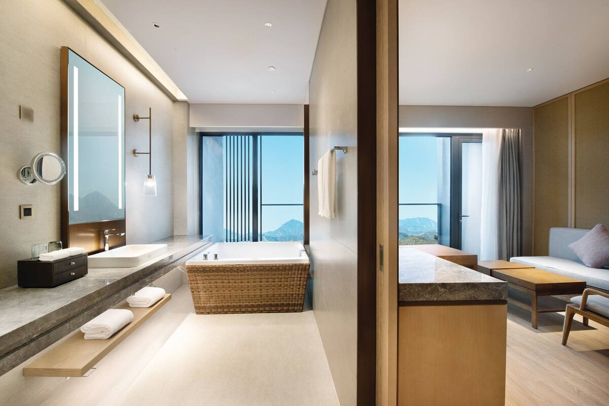 A modern bathroom with a large mirror, two sinks, a bathtub, and a wooden vanity.
