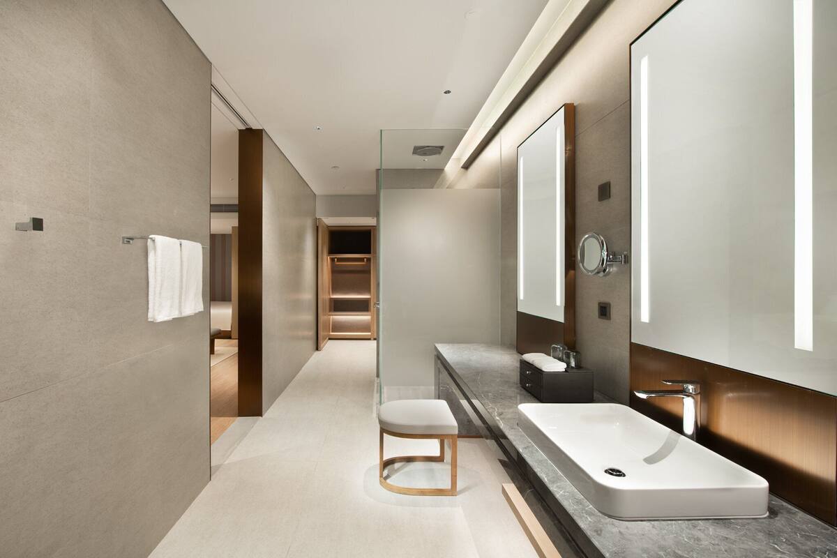 A modern bathroom with a large mirror, a white sink, and a small stool.
