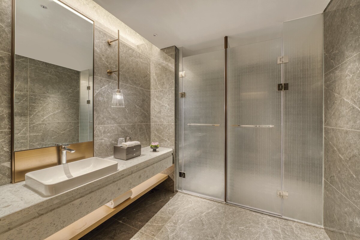 A modern bathroom with a large mirror, two sinks, a shower enclosure, and a wooden vanity.
