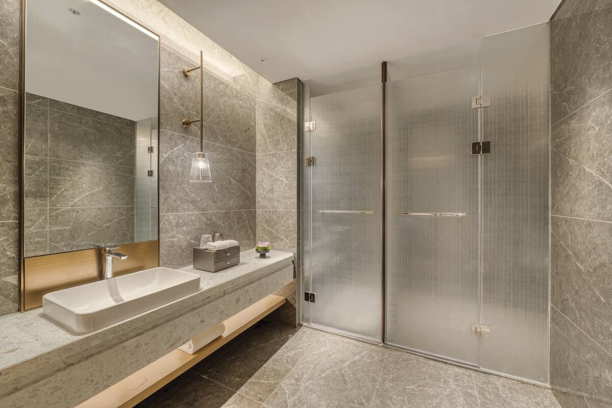 A modern bathroom with a large mirror, two sinks, a shower enclosure, and a wooden vanity.
