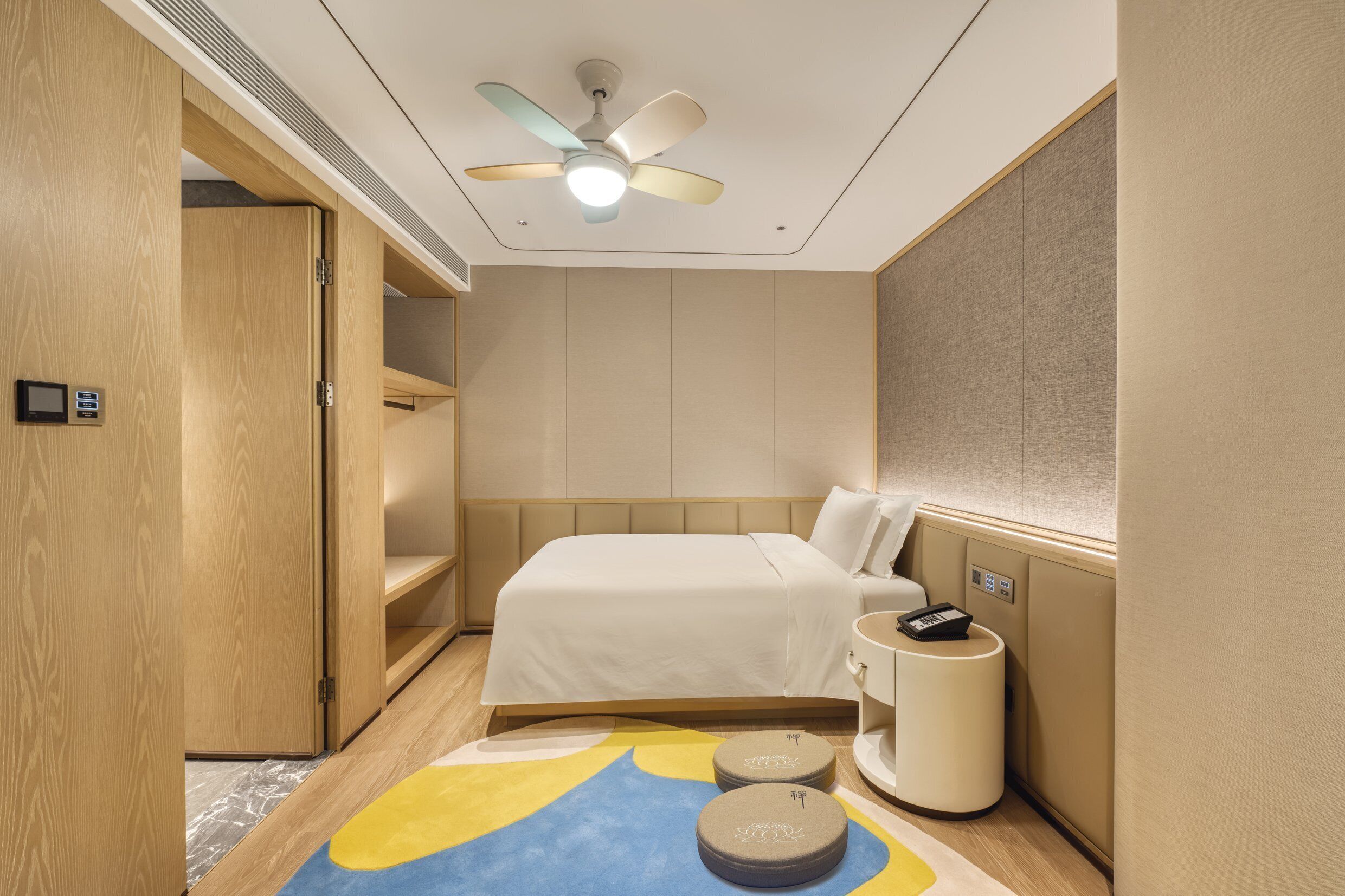 A hotel room with a bed, a bedside table, a nightstand, a ceiling fan, and a small rug.