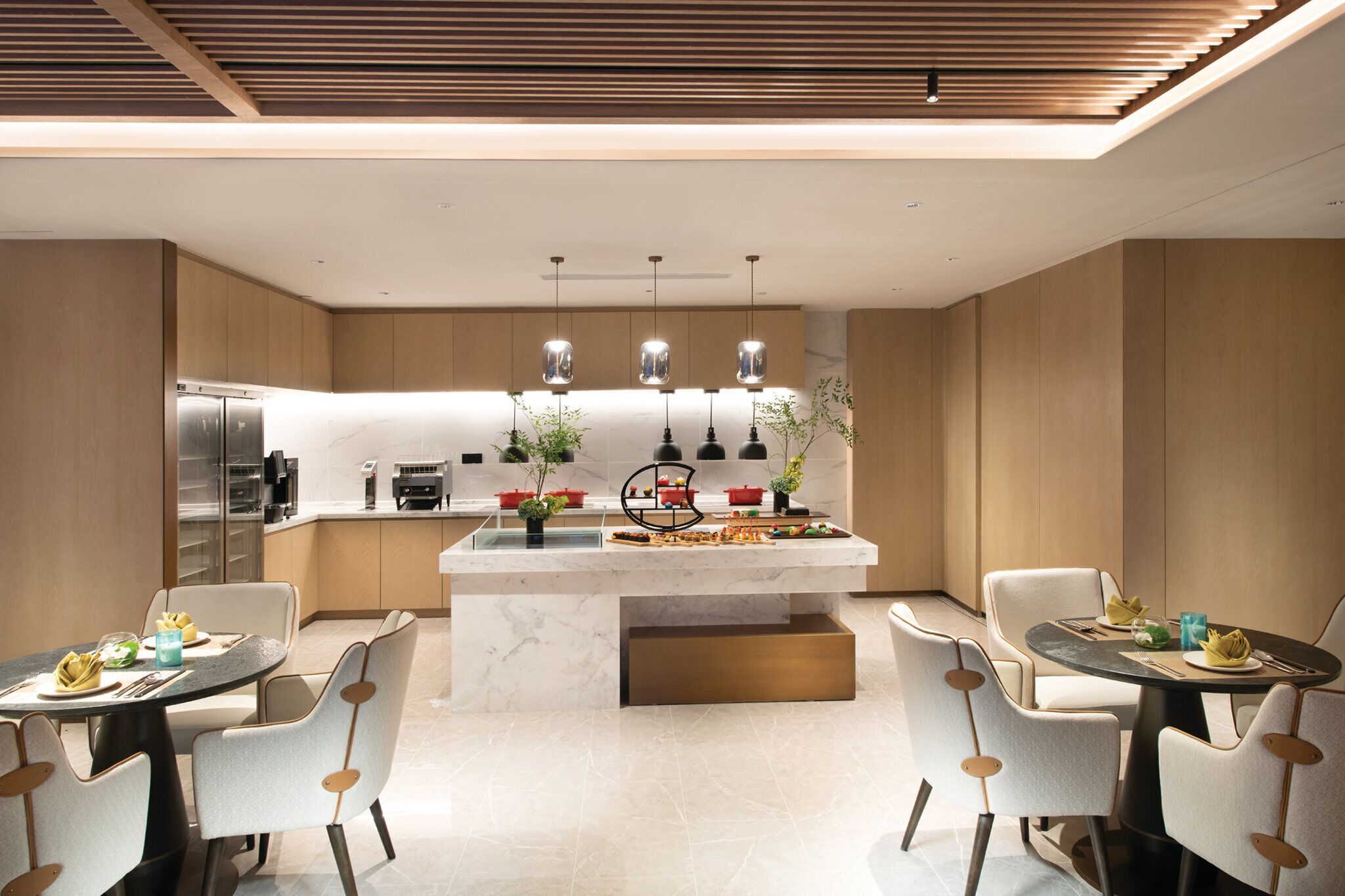 A modern kitchen with a central island, pendant lighting, and a dining area with two tables and chairs.
