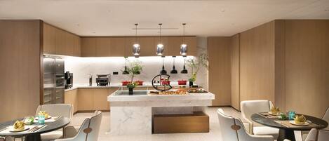 Una cocina moderna con una isla central, iluminación colgante y una zona de comedor con dos mesas y sillas.