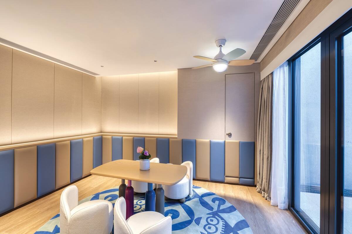 A modern hotel room with a seating area, a ceiling fan, and large windows.