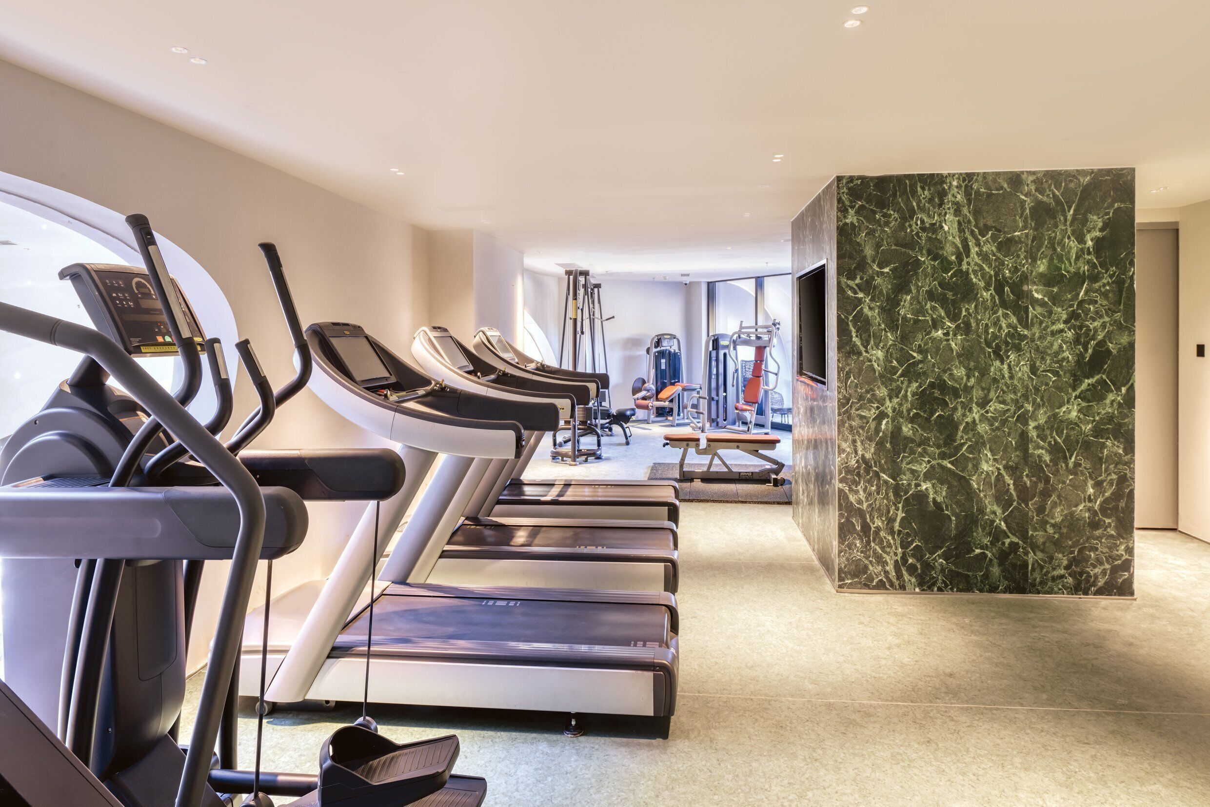 A modern gym with treadmills, elliptical machines, and weight equipment.