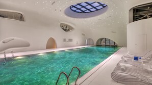 An indoor swimming pool with clear water, a skylight, and lounge chairs. - Crowne Plaza Zunhua Hot Spring Town by IHG (Tangshan)