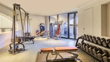 Een fitnessruimte met diverse trainingsapparaten, waaronder banken en gewichten, en een groot raam met uitzicht.