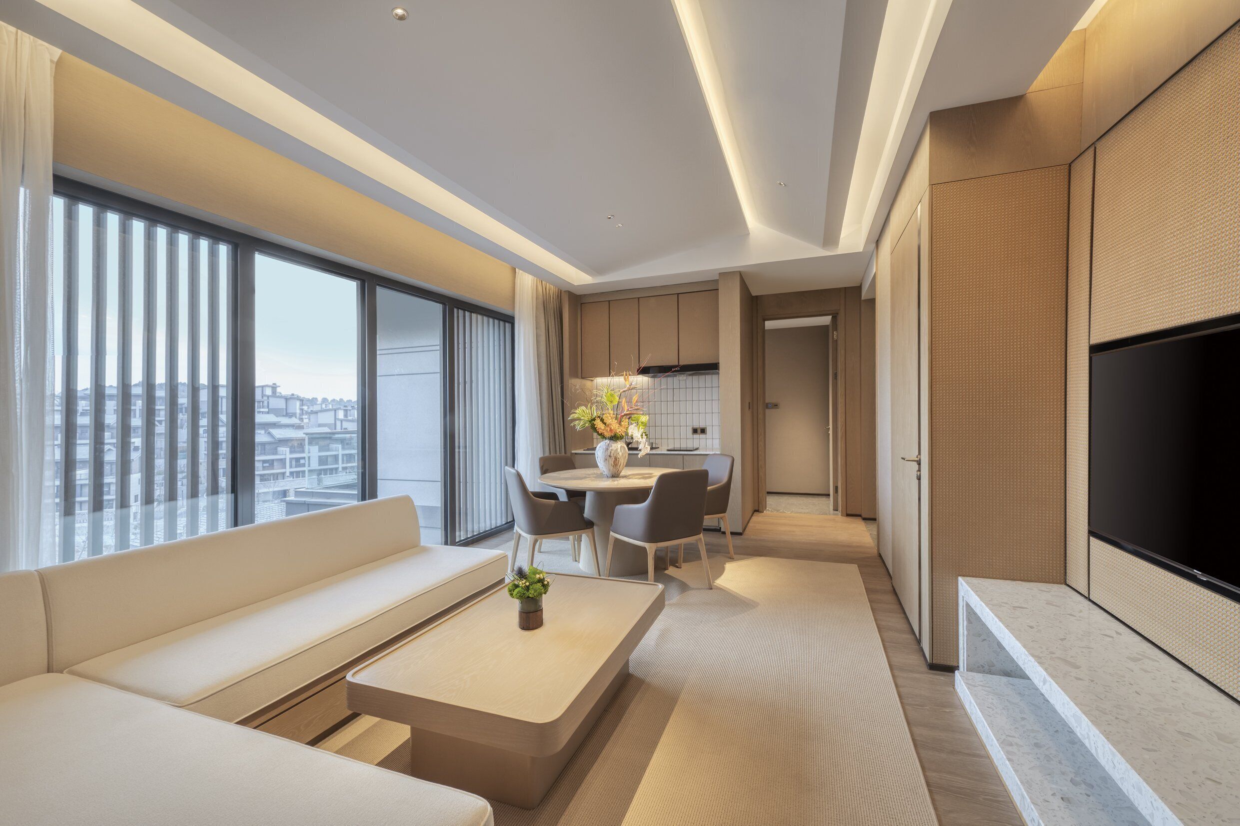 Una sala de estar moderna con sofá, mesa de centro y televisor de pantalla plana. Se observa un comedor con mesa y sillas, y una cocina al fondo.