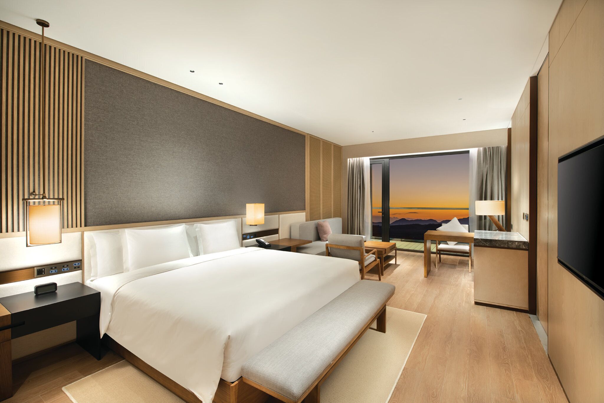 A modern hotel room with a large bed, bedside tables, a desk, and a TV.