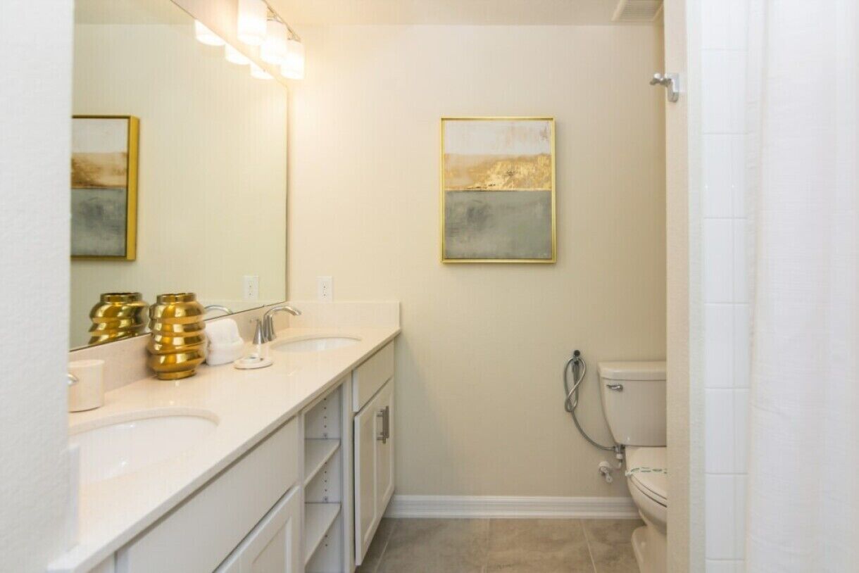 Une salle de bain avec deux lavabos, des toilettes et une douche. Des vases décoratifs sont posés sur le plan de travail du lavabo.