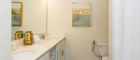 Une salle de bain avec deux lavabos, des toilettes et une douche. Des vases décoratifs sont posés sur le plan de travail du lavabo.