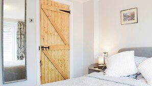Une chambre avec une porte en bois, un lit avec une literie blanche, une table de chevet avec une lampe et un tableau encadré au mur.