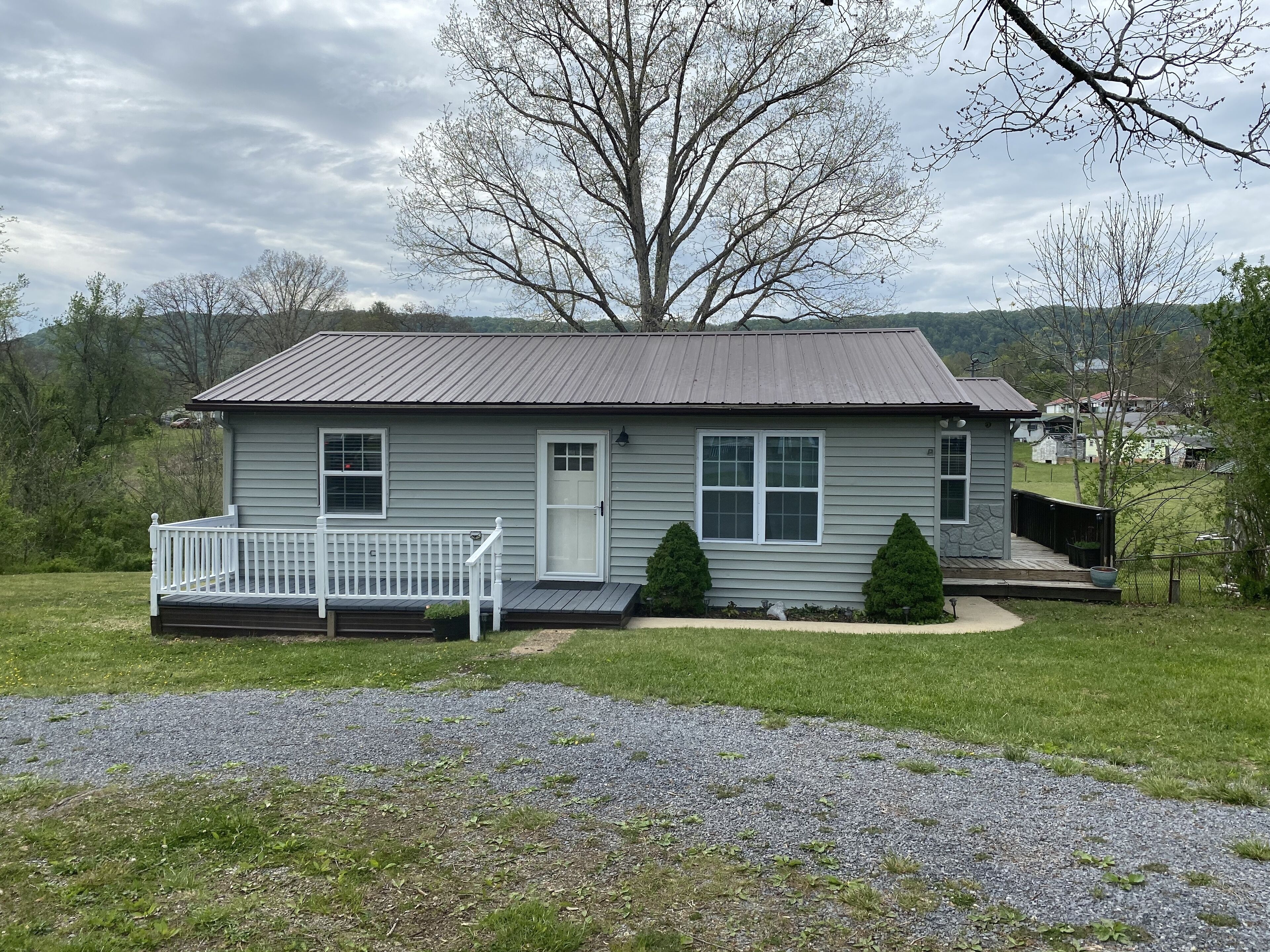 A single-story house with a front porch, a small deck, and a gravel driveway.