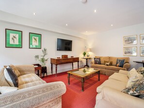 A living room with a red carpet, two sofas, a coffee table, a TV, and framed pictures on the walls.