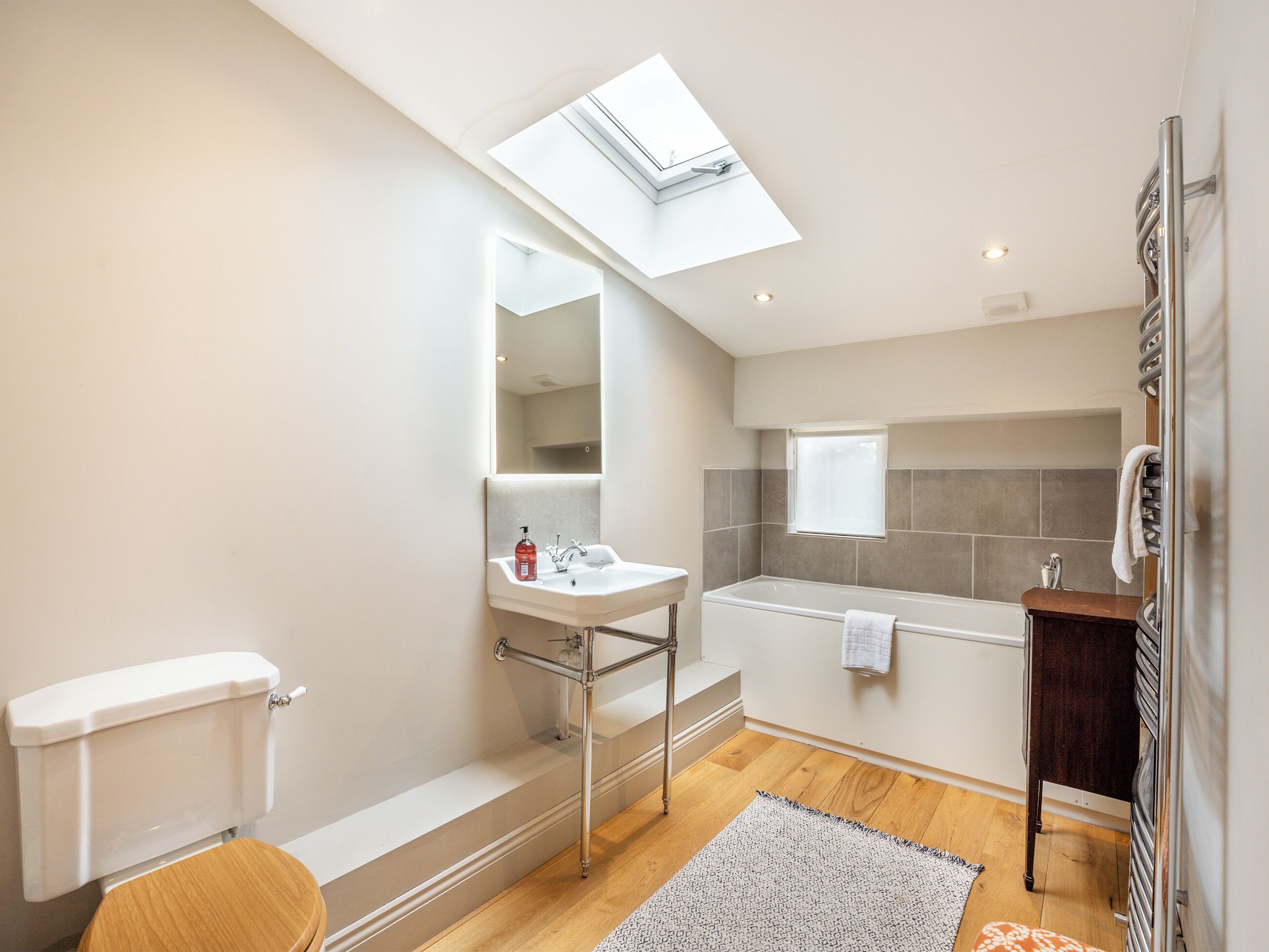 A modern bathroom with a skylight, a bathtub, a toilet, and a sink.