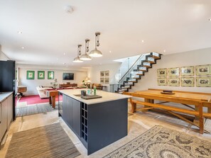 A modern kitchen with a central island, a dining area with a wooden table, and a staircase leading to an upper level.
