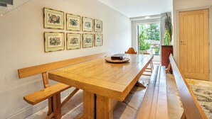 Un vaste espace dédié à la salle à manger, avec une longue table en bois entourée de chaises, et un escalier menant à un niveau supérieur.