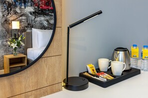 Quarto de hotel com espelho redondo, abajur, bandeja com xícaras de café e lanches, e cafeteira.
