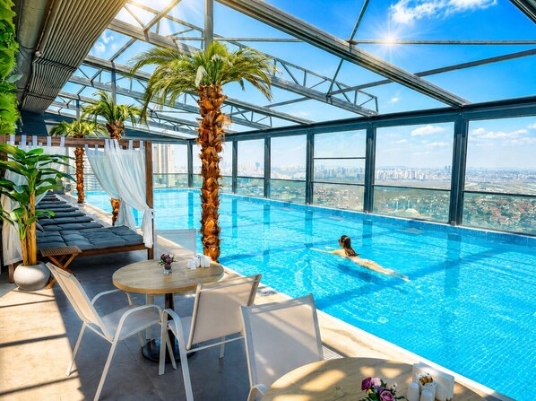 Una piscina infinita en el interior con vistas a la ciudad, sillones de descanso y una mesa con un florero.