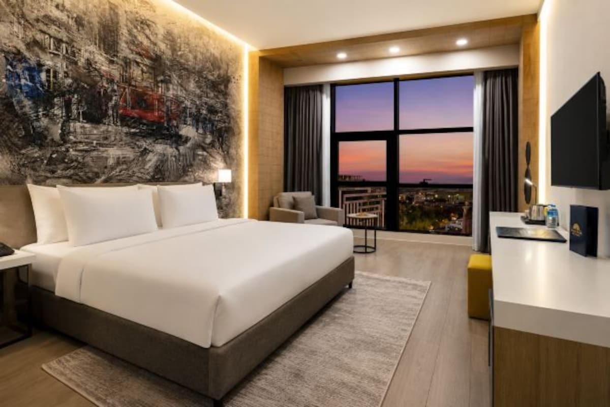 A modern hotel room with a large bed, a city view, a desk, and a TV.