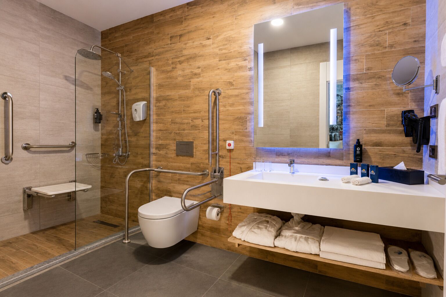 Een moderne badkamer met douche, toilet en wastafel, met houten wandpanelen en een grote spiegel.