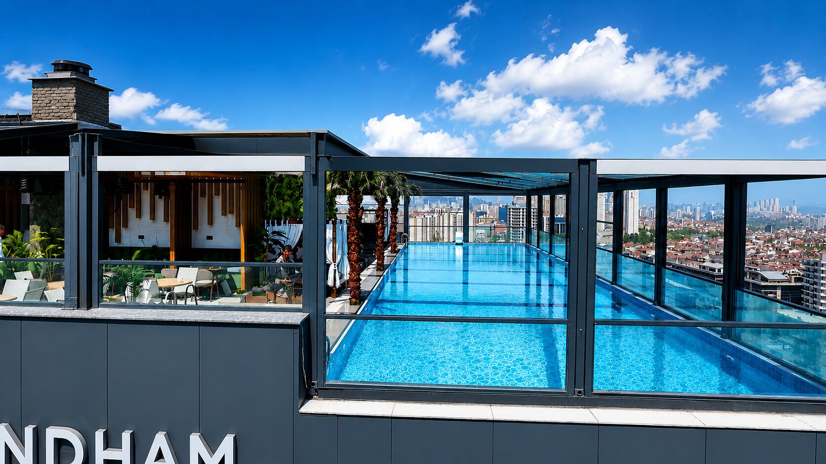 Una piscina en la azotea con vistas a la ciudad, una zona de estar al aire libre techada y un edificio con letreros 'NDHAM'.