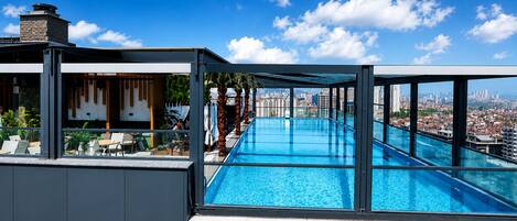 Una piscina en la azotea con vistas a la ciudad, una zona de estar al aire libre techada y un edificio con letreros 'NDHAM'.