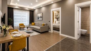 Ein modernes Wohnzimmer mit Sofa, Esstisch und Stühlen, ein separates Schlafzimmer mit Bett sowie ein durch eine offene Tür einsehbarer Badezimmer.