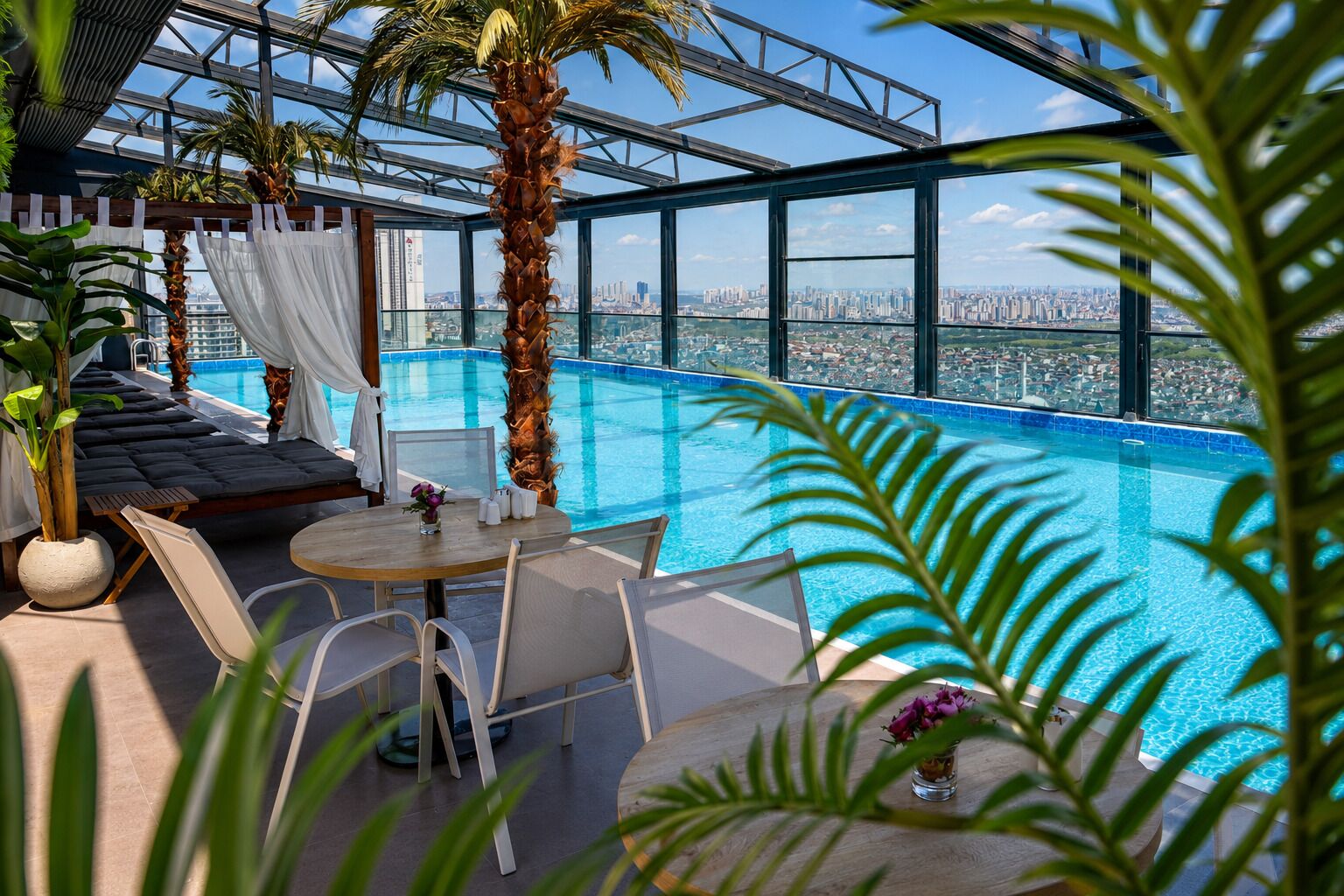 Une piscine à débordement située sur le toit, offrant une vue sur la ville, avec des espaces de détente et des plantes en pot.