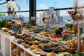 Un buffet proposant une variété de plats, avec une vue sur le paysage urbain grâce à de grandes fenêtres.