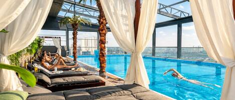 A rooftop infinity pool with a city view, sun loungers, and palm trees.