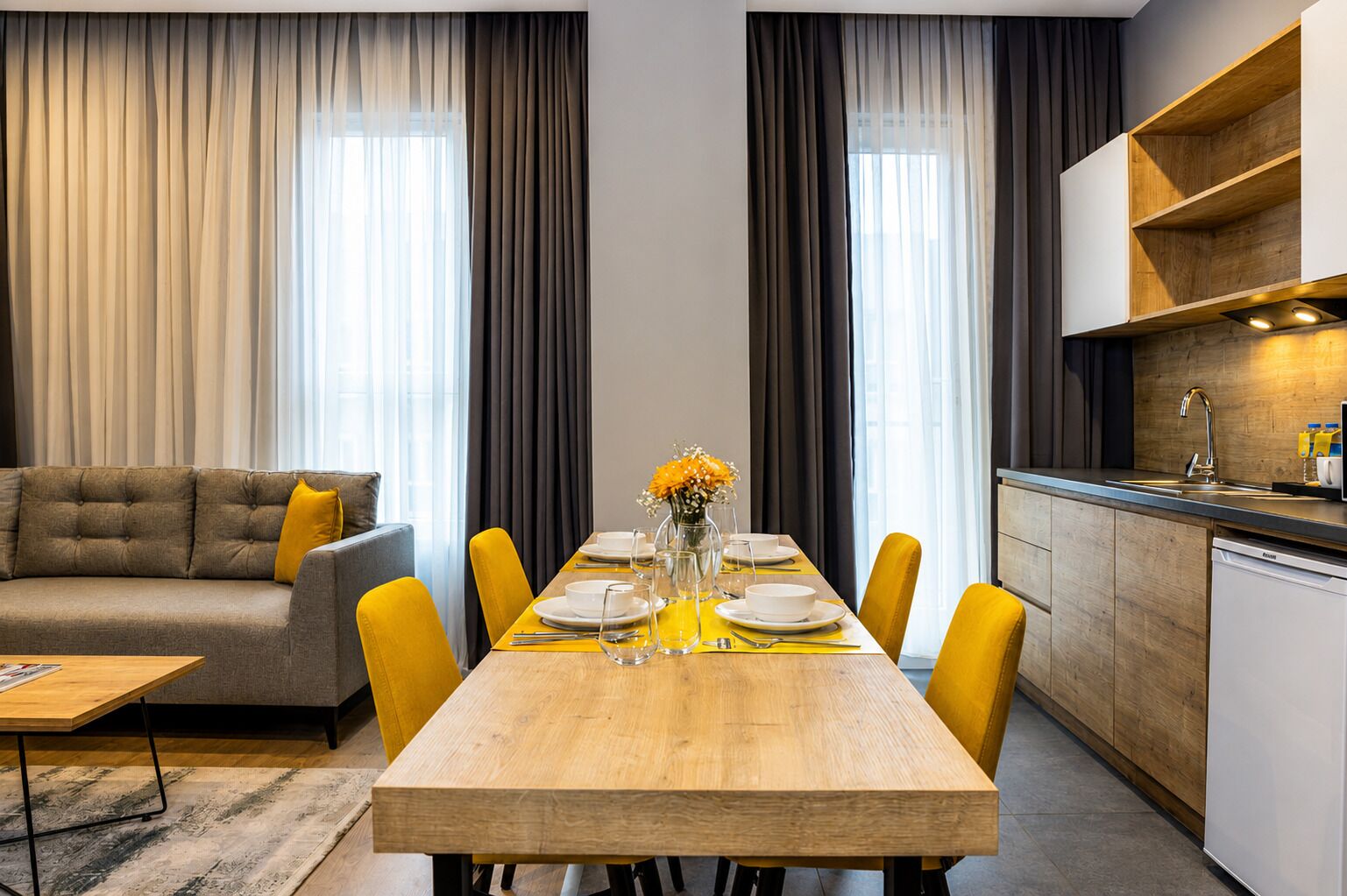A modern living room with a sofa, dining table, and kitchen area.