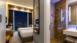 Ein Hotelzimmer mit Bett, Schreibtisch, Fernseher, Blick auf die Stadt und einer Duschgelegenheit.