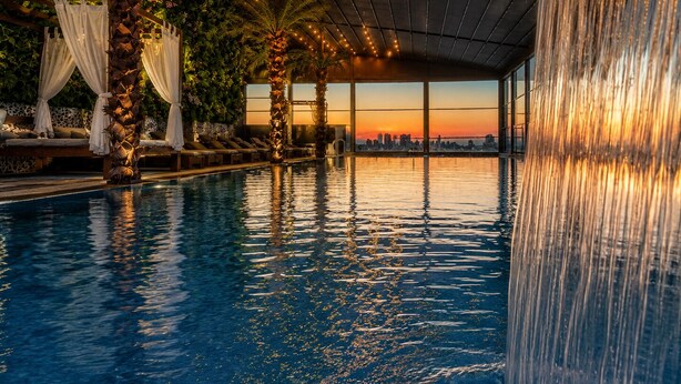 Ein Innenpool mit Sonnenuntergangsblick, Palmen und einem Wasserfall.