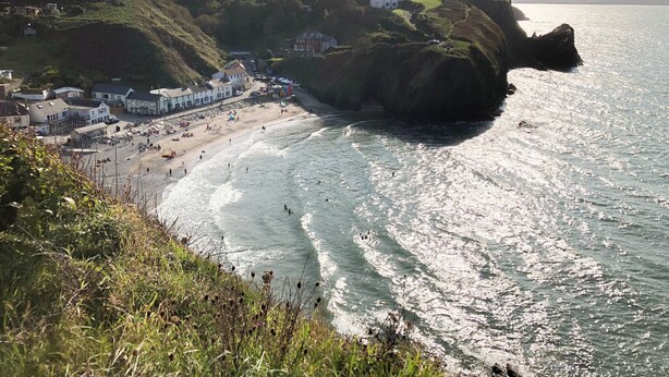 A coastal town with buildings along the beach, a cliff overlooking the sea, and a clear view of the coastline.