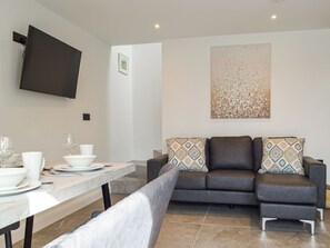 Un salon moderne avec un canapé, un téléviseur à écran plat fixé au mur et une table à manger dressée avec de la vaisselle blanche.
