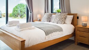 A modern bedroom with a wooden bed, two bedside tables, a nightstand, and a view of the outdoors.