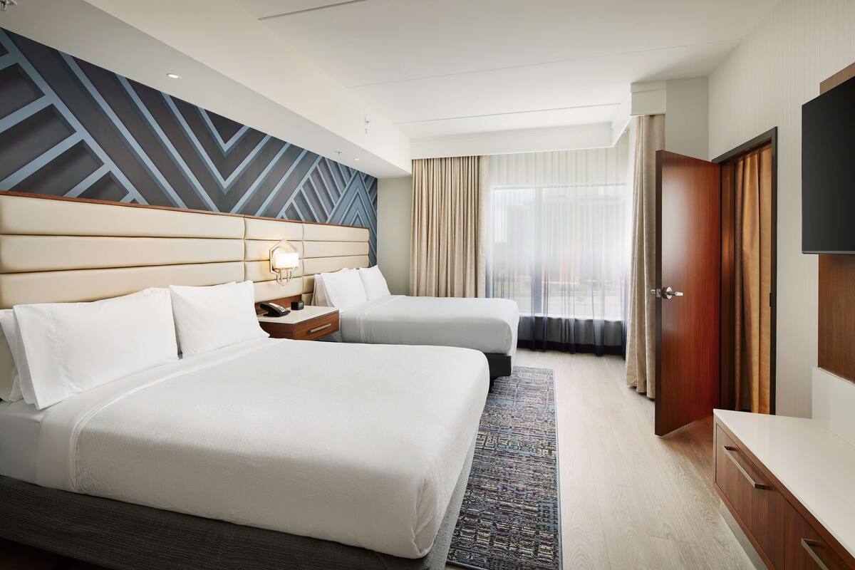 Een hotelkamer met twee bedden, een grote spiegel, een televisie en een raam met gordijnen.