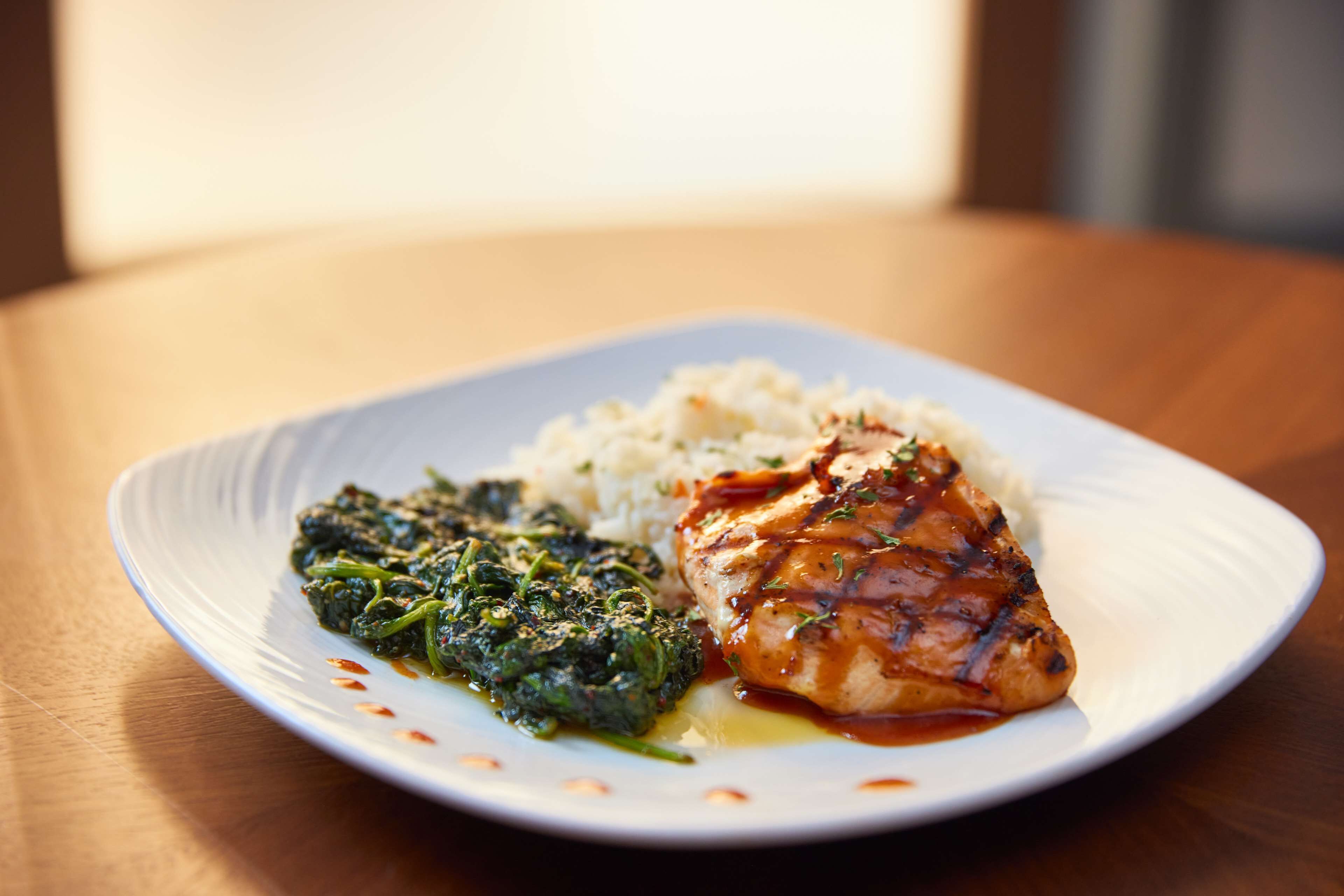 A plate with grilled chicken, rice, and spinach on a white plate.