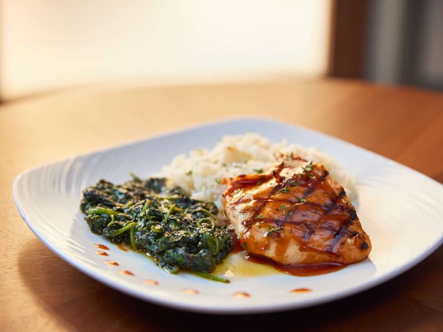 A plate with grilled chicken, rice, and spinach on a white plate.