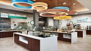 Un espace buffet avec plusieurs points de service, une cuisine en arrière-plan et un panneau indiquant : « Spécialités de saison ».