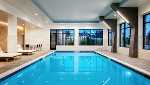 Une piscine intérieure moderne avec une eau d’un bleu limpide, de grandes fenêtres et un espace détente équipé de chaises longues.