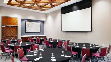 A conference room with multiple tables and chairs, a large screen, and a wooden ceiling.