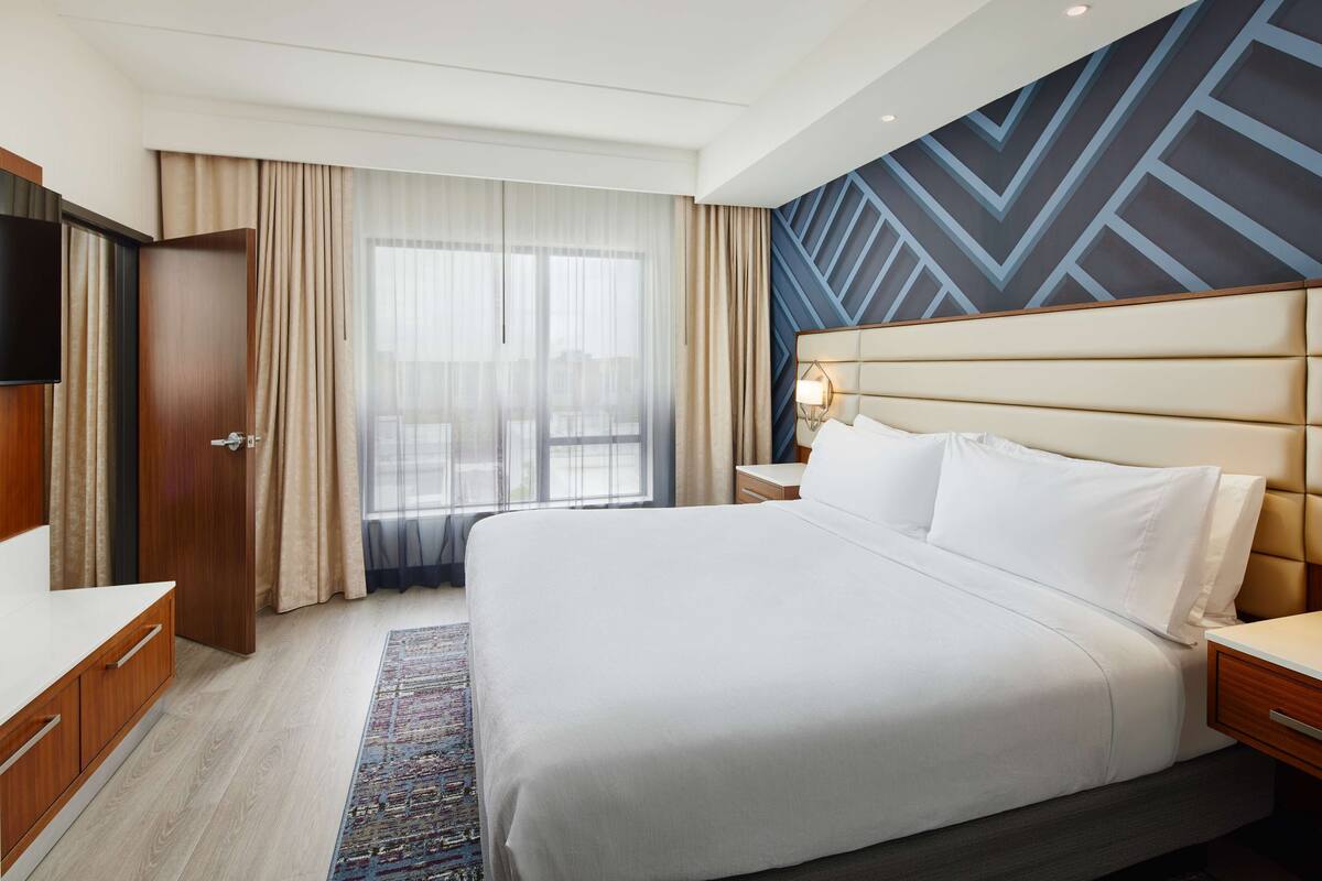 Een hotelkamer met een groot bed, een houten dressoir, een televisie en uitzicht op de stad.