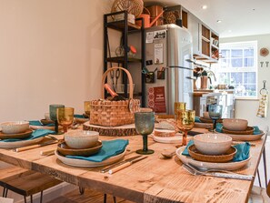 Uma mesa de jantar de madeira posta com tigelas, pratos e talheres, com uma cesta e uma garrafa sobre ela.