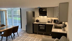 A modern kitchen with a built-in oven, a microwave, and a toaster. There is a dining table with chairs and a sofa in the living area. - Newly converted barn with hot tub,stylish interior and outdoor space (Roundthwaite)
